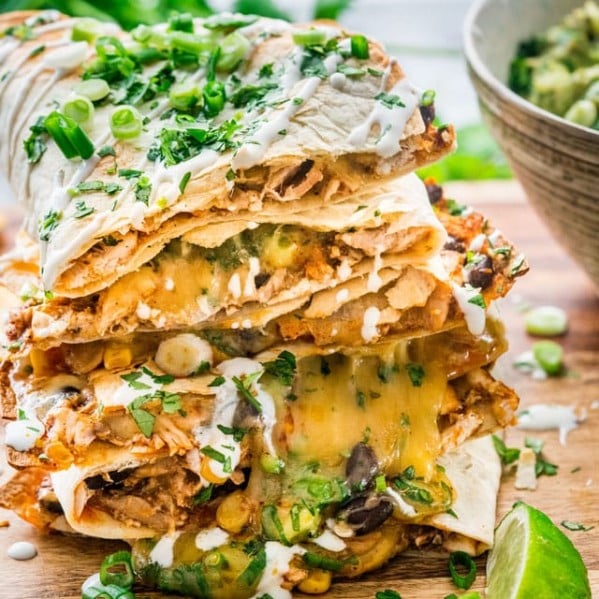 a stack of chicken enchilada quesadillas on a cutting board with a garnish of lime wedge