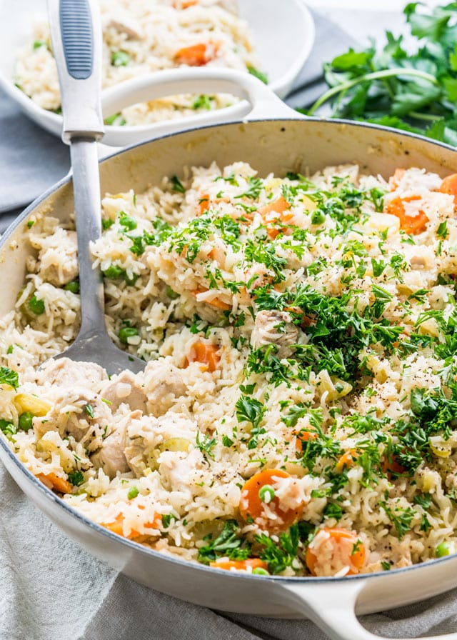 chicken rice pilaf in a skillet with a spoon inside the skillet garnished with parsley