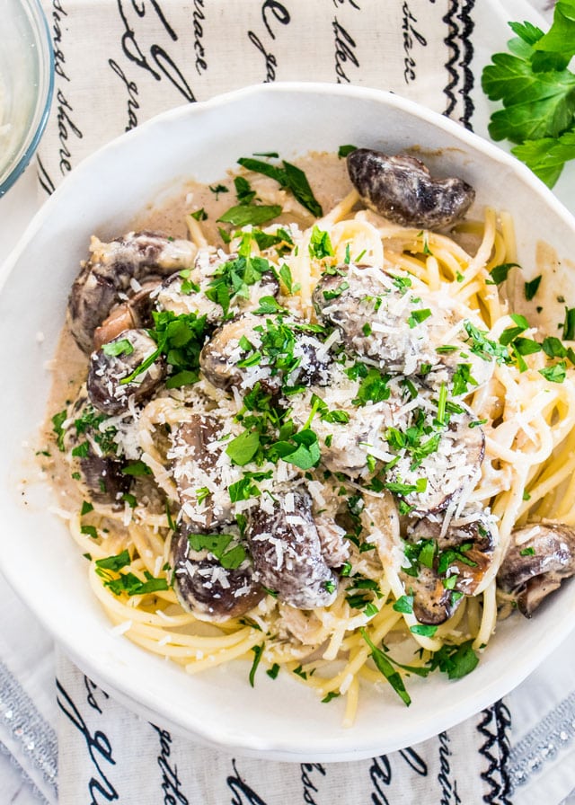 overhead shot of creamy garlic parmesan mushrooms over pasta in a white plate