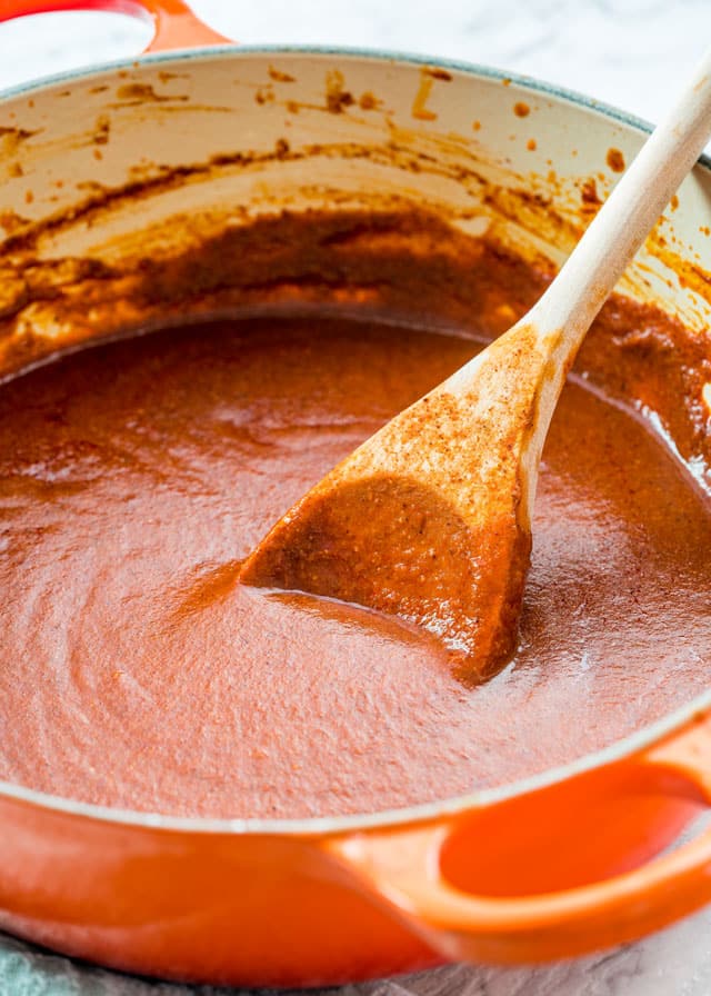 enchilada sauce in a Dutch oven with a wooden spoon