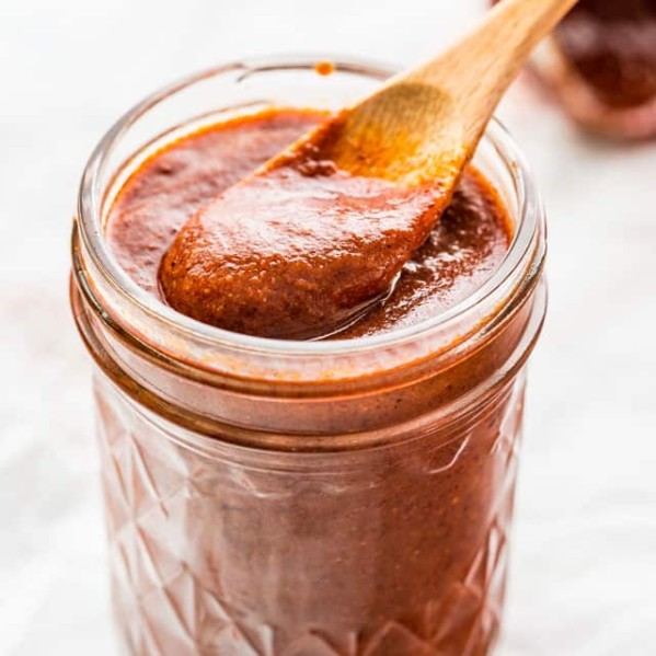 side view shot of a small wooden spoon taking a scoop of enchilada sauce from the jar