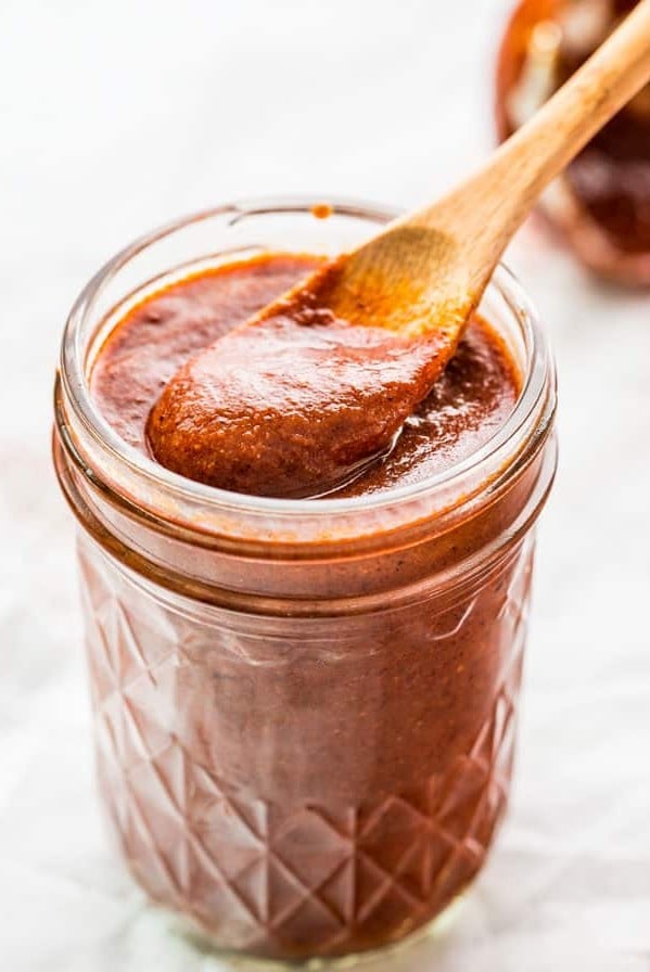 side view shot of a small wooden spoon taking a scoop of enchilada sauce from the jar