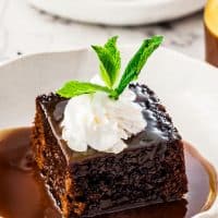 side view shot of a slice of sticky toffee pudding in a bowl topped with a dollop of whipped cream and a sprig of mint