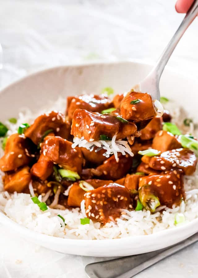a fork holding instant pot general tso's chicken over a plate with white rice