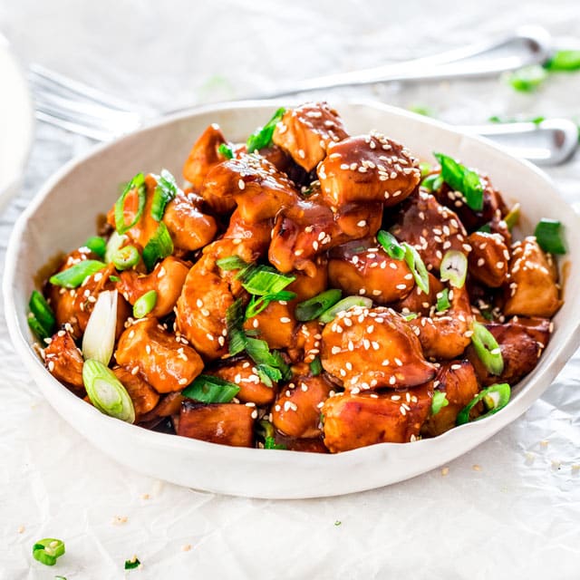 a white bowl filled with instant pot general tso's chicken garnished with green onions and sesame seeds
