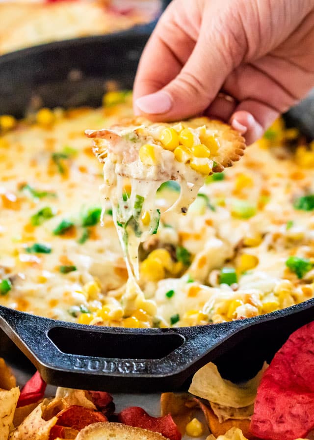 Finished bacon corn dip in a skillet with a cracker dipping in for a bite
