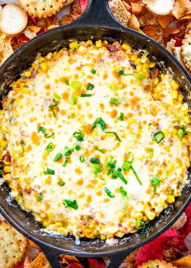 Bacon corn dip in a skillet garnished with green onion with crackers and tortilla chips along the side