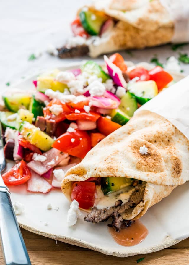 Finished beef brisket gyro served on a white plate with greek salad on the side
