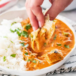 side view shot of a hand dipping a piece of naan bread into the bowl of chicken tikka masala