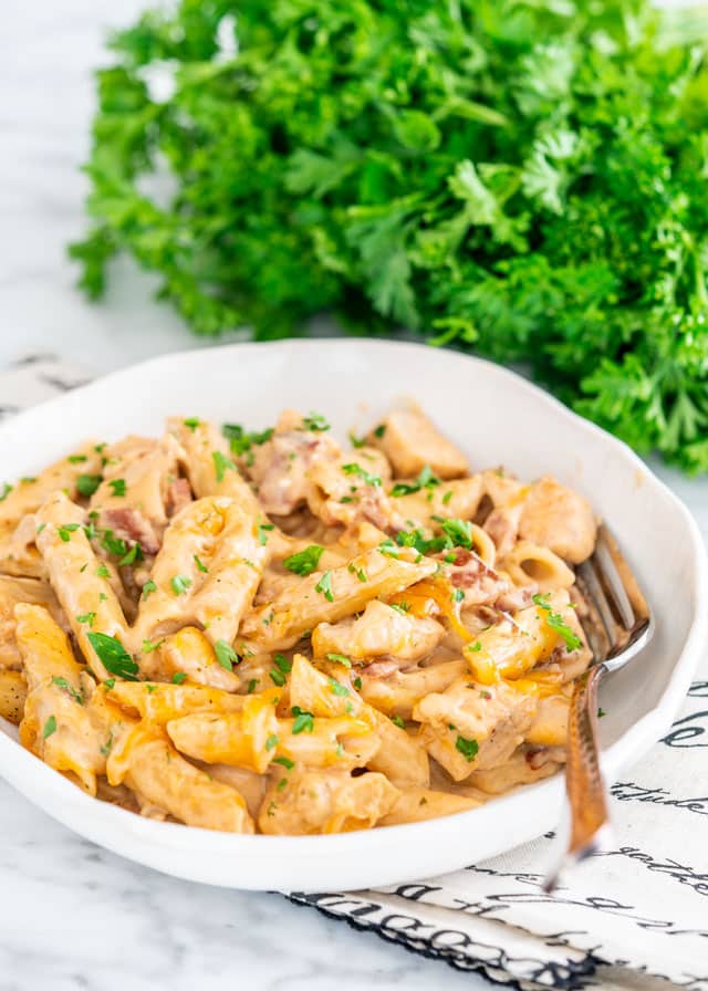 Crack Chicken Penne in a white plate with a fork and parsley in the background