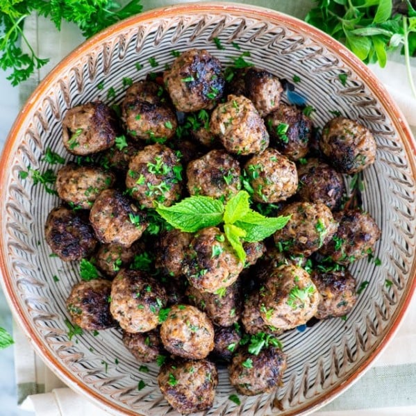overhead shot of a bowl of greek meatballs surrounded by fresh herbs