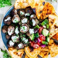 overhead shot of greek meatballs topped with tzatziki on a plate with pita bread and greek salad