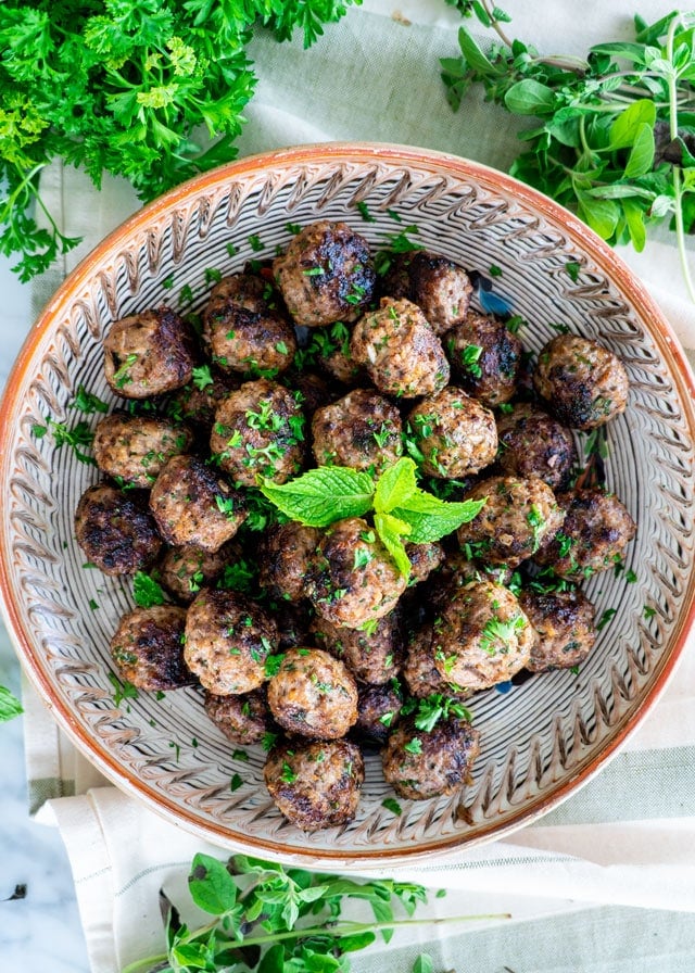 overhead shot of a bowl of greek meatballs surrounded by fresh herbs