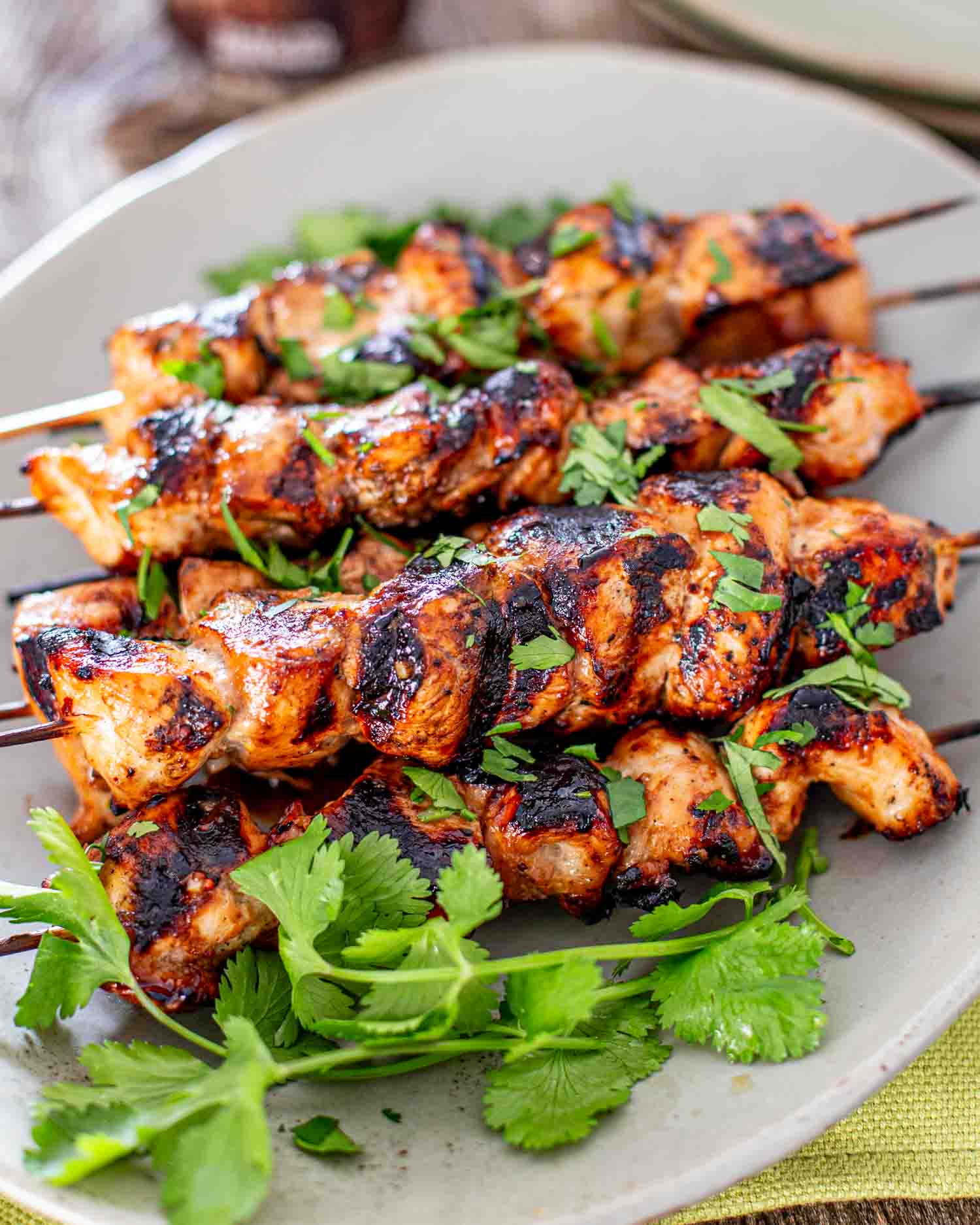 a few honey beer bbq chicken skewers on a white platter garnished with cilantro.