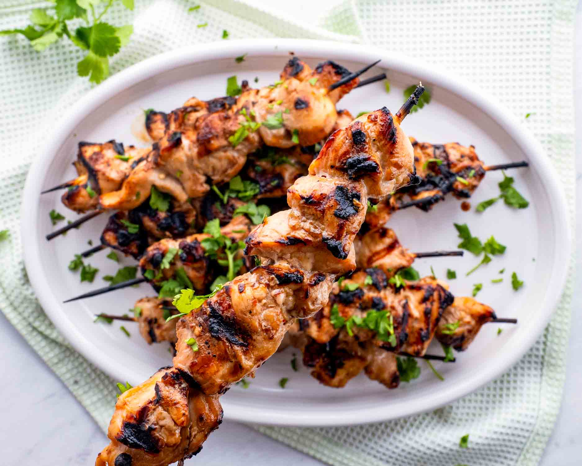 a few honey beer bbq chicken skewers on a white platter garnished with cilantro.