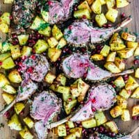 overhead shot of herb crusted rack of lamb surrounded by roasted potatoes. Garnished with pomegranate seeds