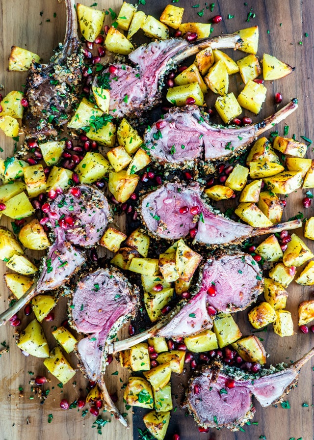 overhead shot of herb crusted rack of lamb surrounded by roasted potatoes. Garnished with pomegranate seeds