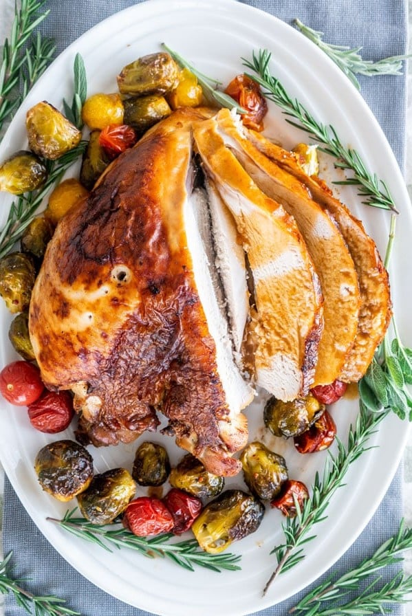 overhead shot of sliced brined roast turkey breast surrounded by roasted veggies and rosemary sprigs on a serving plate