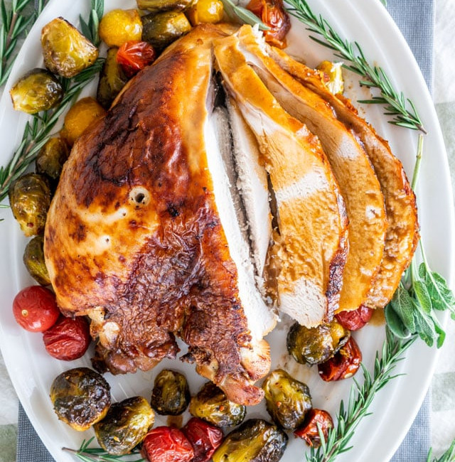 overhead shot of sliced brined roast turkey breast surrounded by roasted veggies and rosemary sprigs on a serving plate