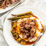 overhead shot of slow roasted leg of lamb on a plate with mashed potatoes brussel sprouts and asparagus