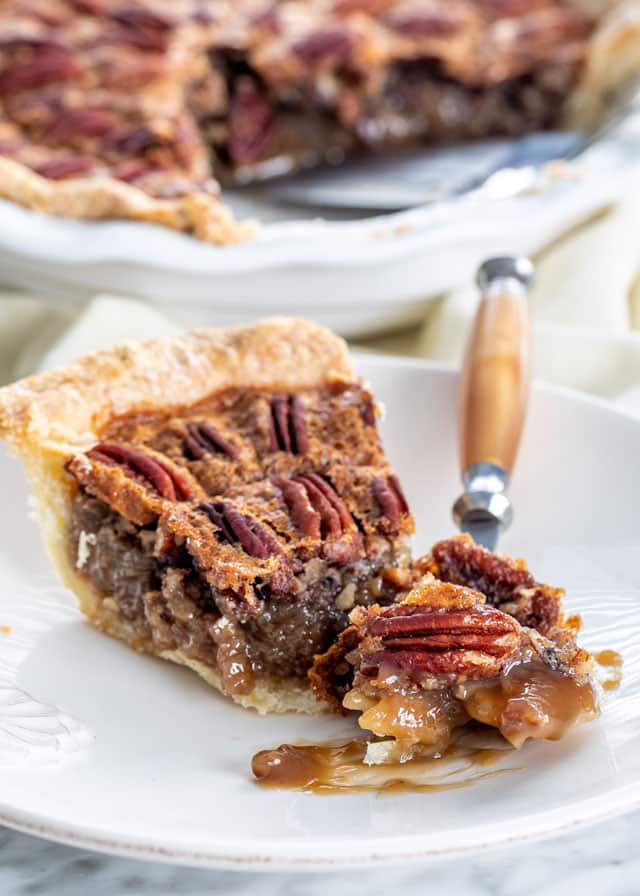 a slice of pecan pie on a white plate with a bite taken out of it