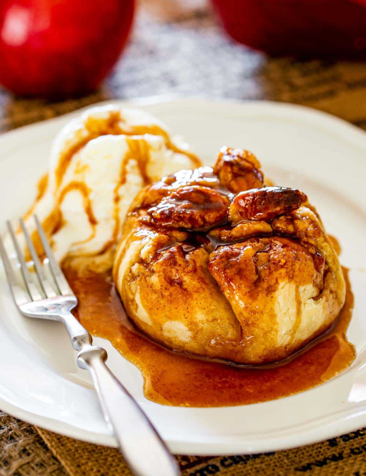 an apple dumpling with a tasty syrup drizzled over it and a scoop of ice cream in white plate