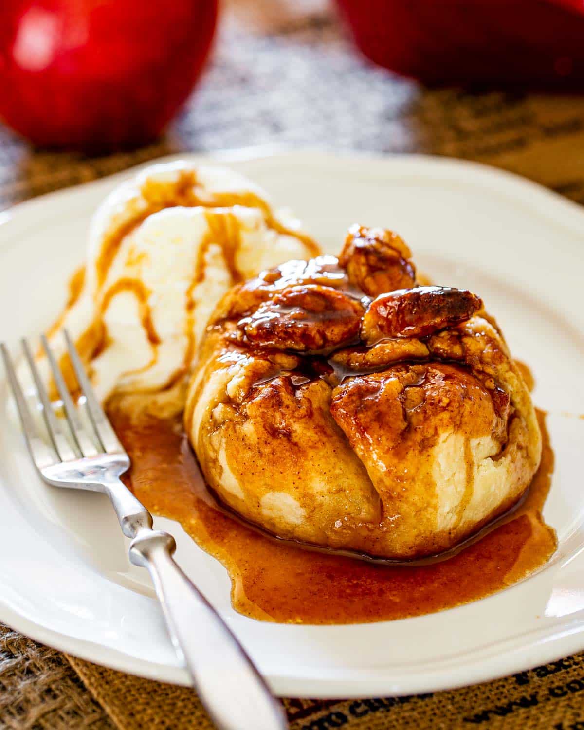 an apple dumpling with a tasty syrup drizzled over it and a scoop of ice cream in white plate