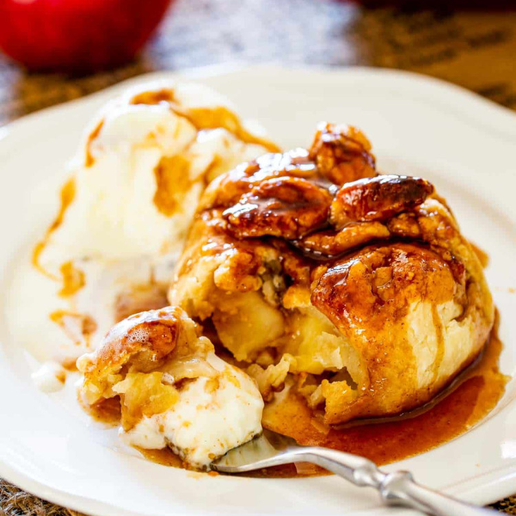 an apple dumpling with a tasty syrup drizzled over it and a scoop of ice cream, and a bite on a fork