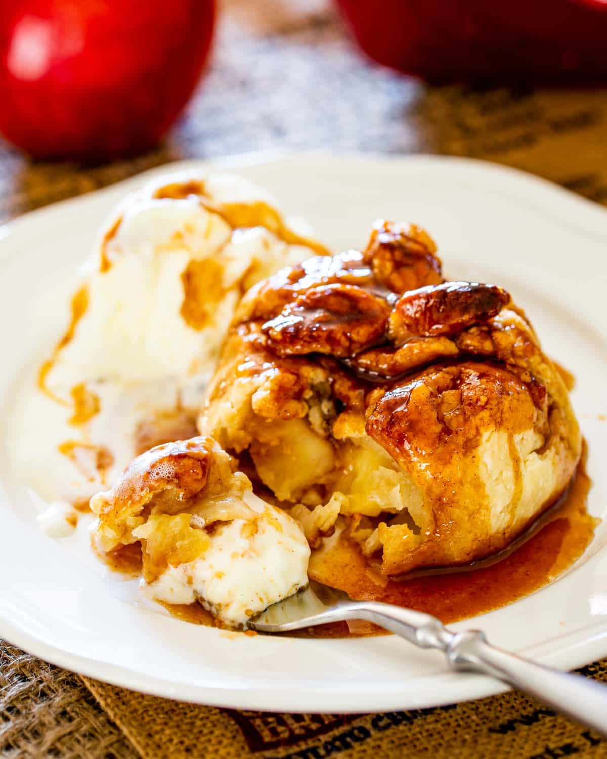 an apple dumpling with a tasty syrup drizzled over it and a scoop of ice cream, and a bite on a fork 
