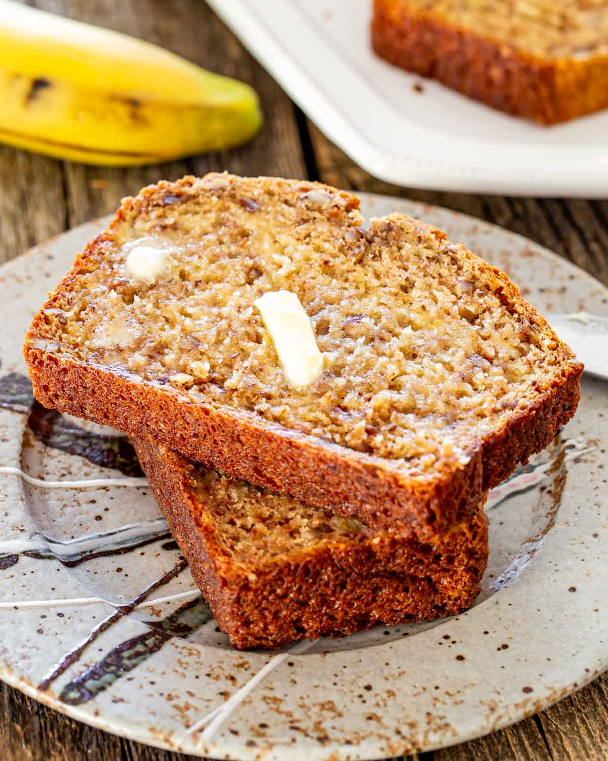 two slices of banana bread on a plate with a pat of butter.