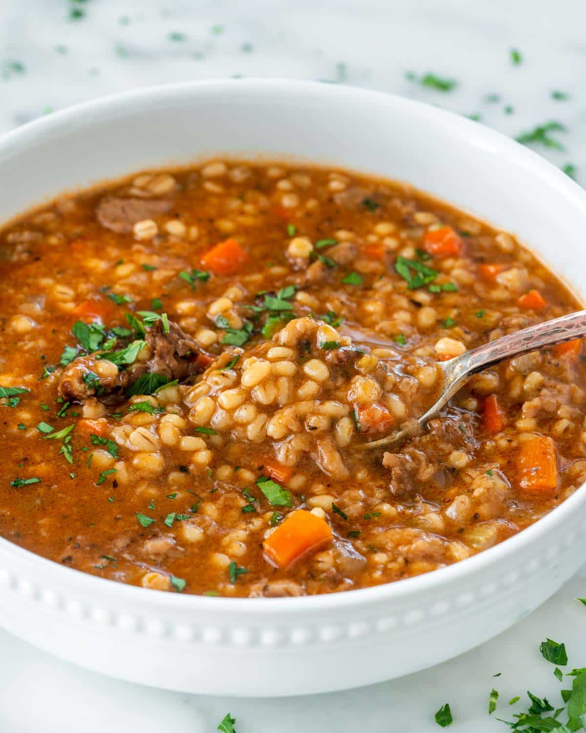beef barley soup in a white bowl with a spoon inside.