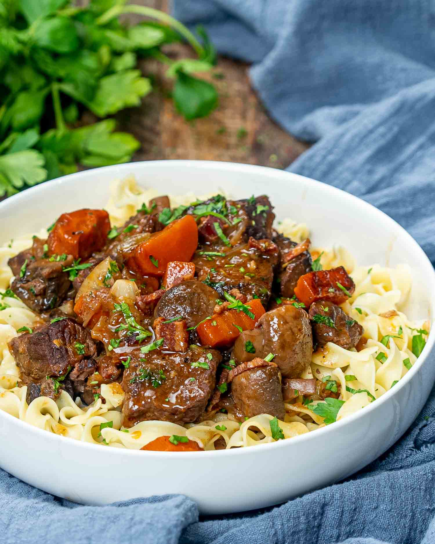 a serving of beef bourguignon over noodles in a white bowl.