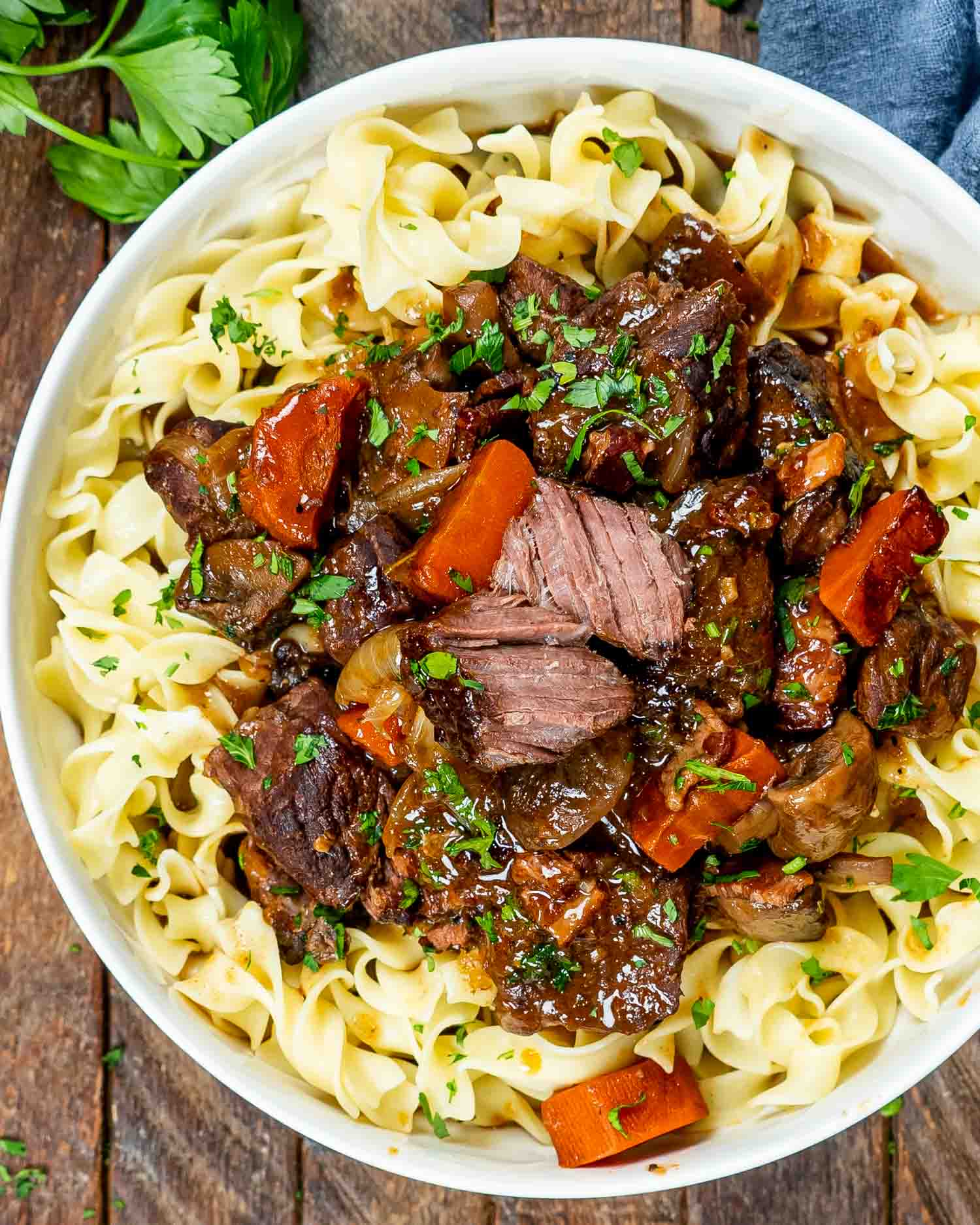 a serving of beef bourguignon over noodles in a white bowl.