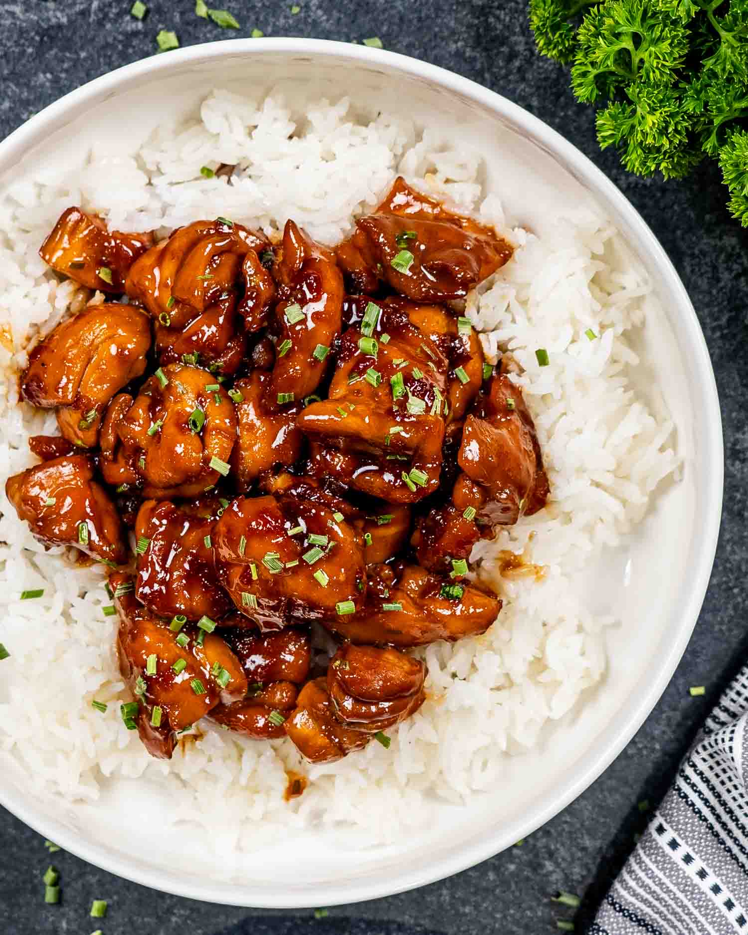a serving of bourbon chicken over a bed of rice in a white bowl.