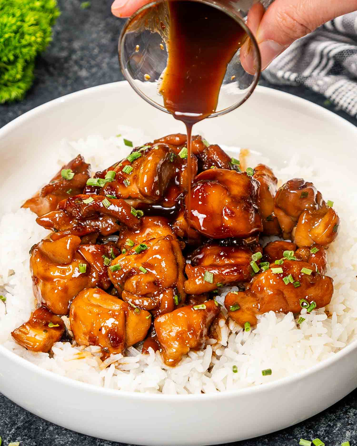 a serving of bourbon chicken over a bed of rice in a white bowl.