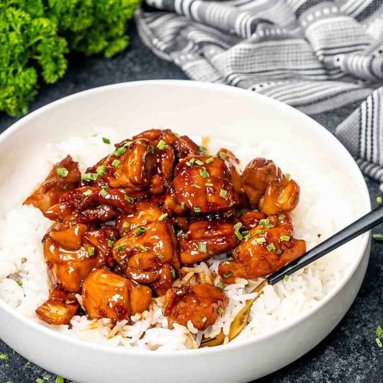 a serving of bourbon chicken over a bed of rice in a white bowl.