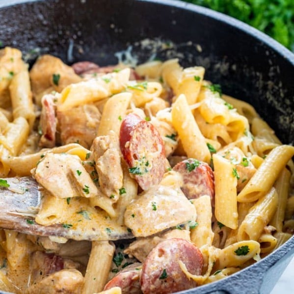 side view shot of a wooden spoon taking a scoop of cajun chicken pasta from a skillet