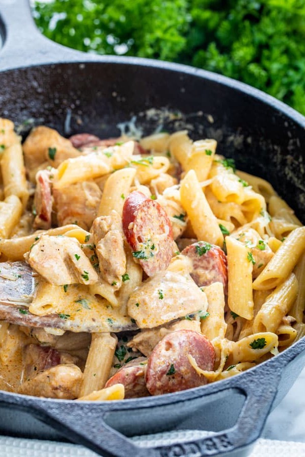 side view shot of a wooden spoon taking a scoop of cajun chicken pasta from a skillet