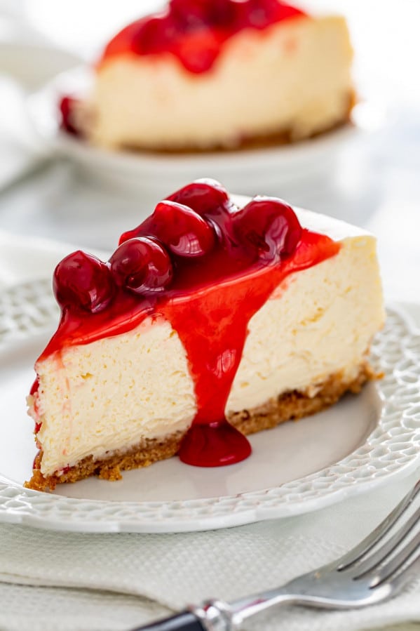 a cheesecake slice with cherry topping on a plate with a fork.