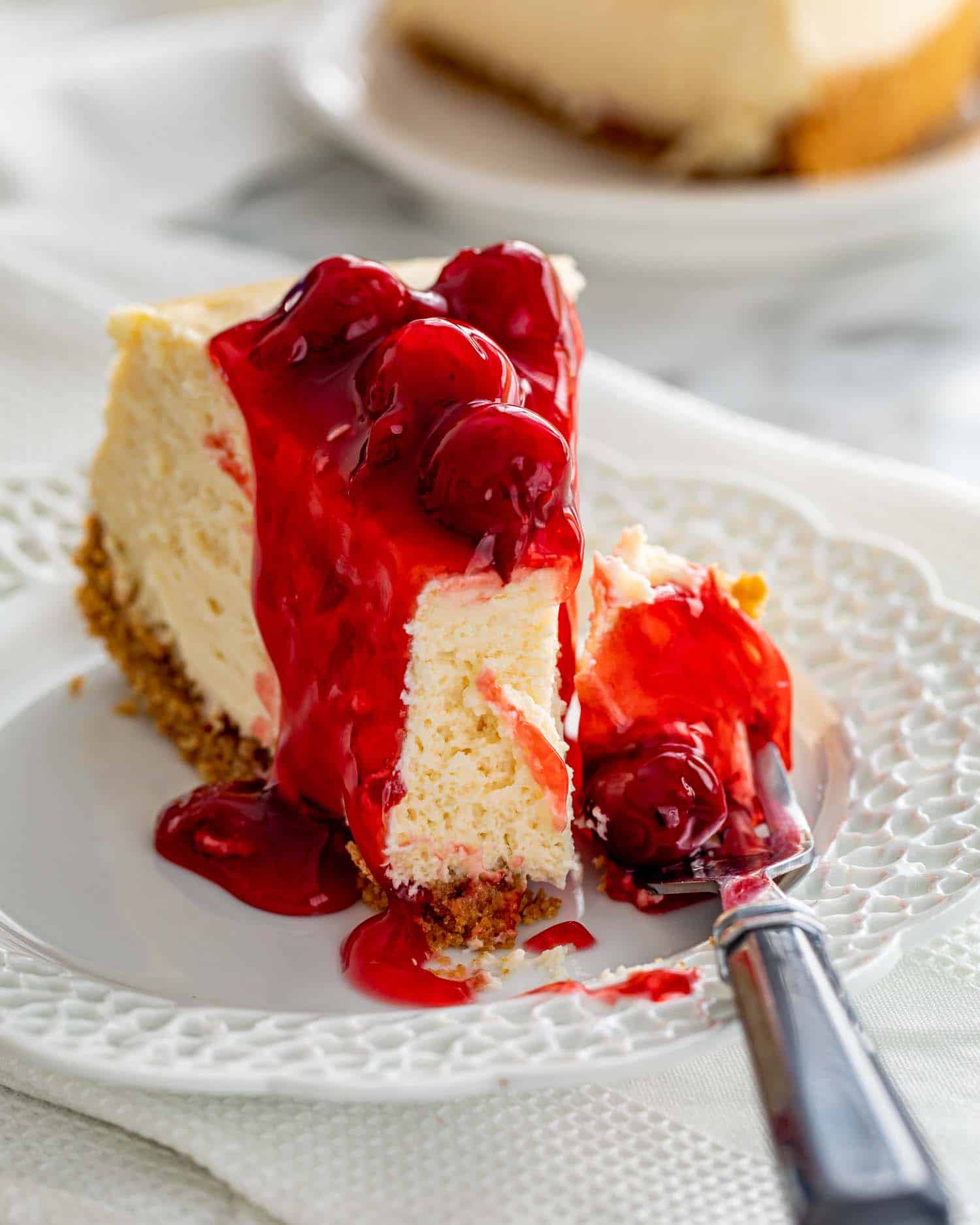 a cheesecake slice with cherry topping on a plate with a fork.