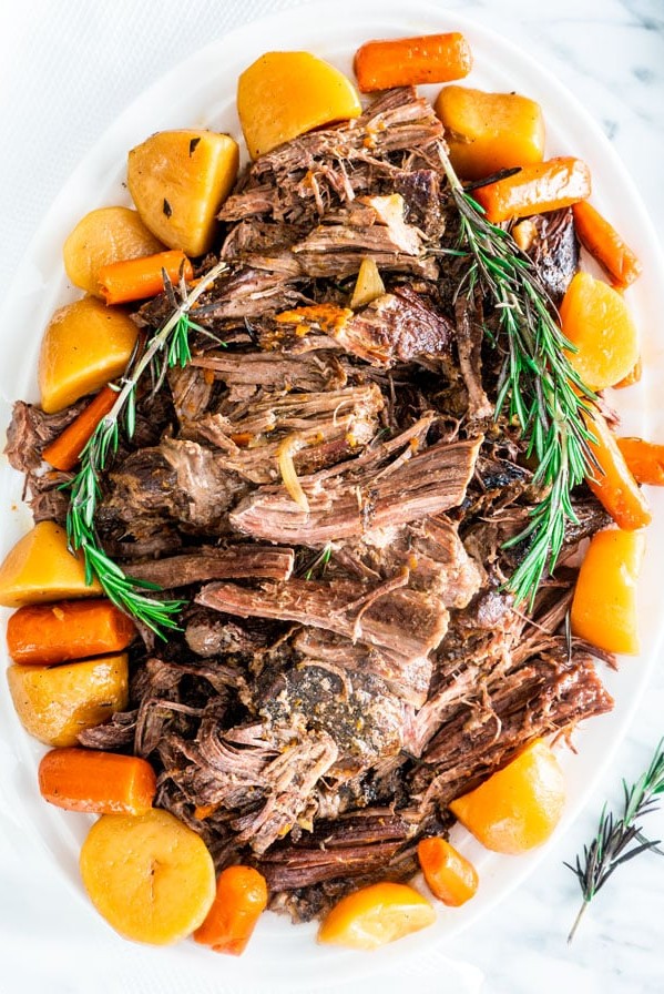overhead shot of a crockpot roast on a large serving platter surrounded by potatoes and carrots