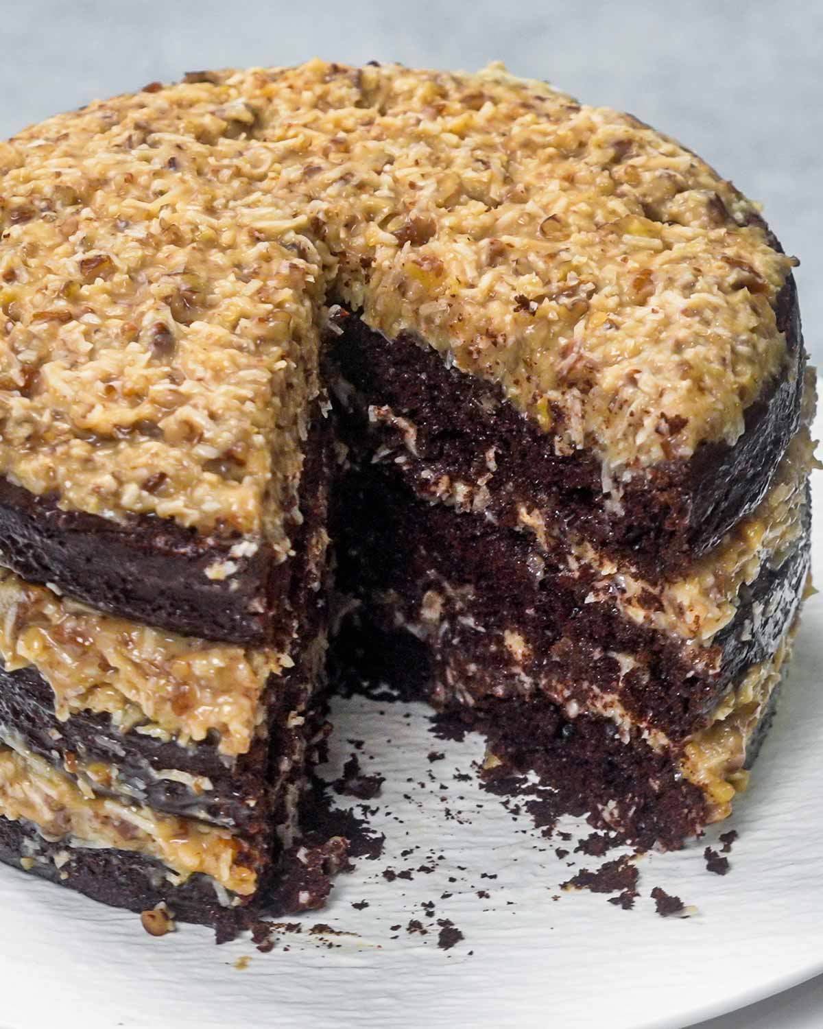 a german chocolate cake on a white platter with a slice removed from it.
