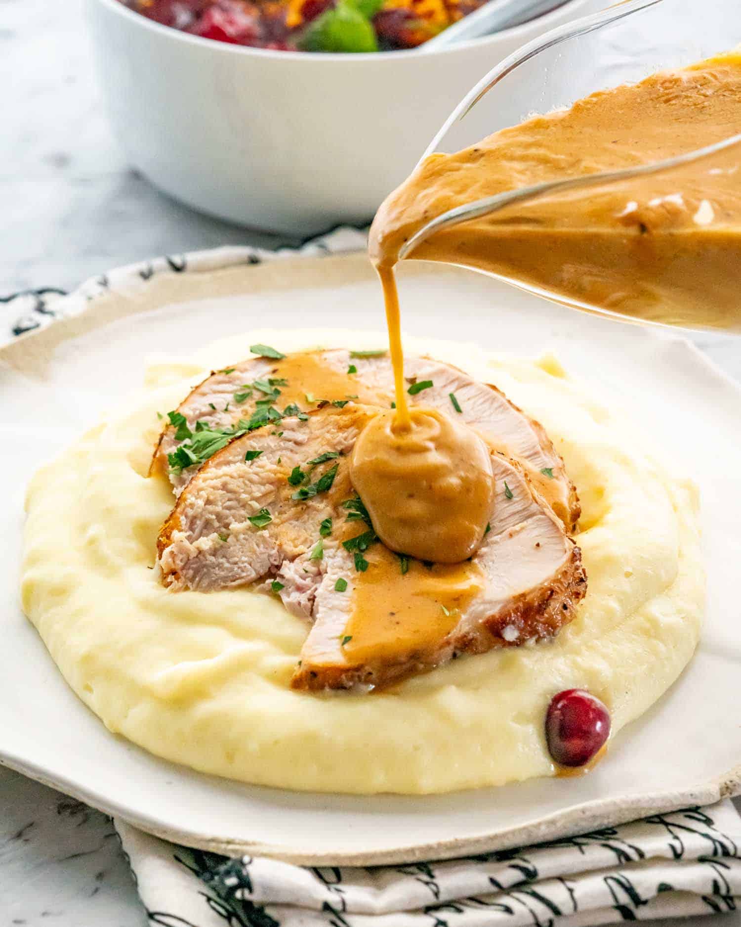 a hand pouring gravy over turkey breast and mashed potatoes.