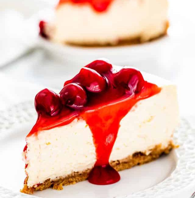 side view shot of a slice of new york style cheesecake with cherry topping on a plate