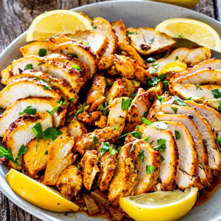 chicken shawarma sliced on a plate garnished with lemon wedges.