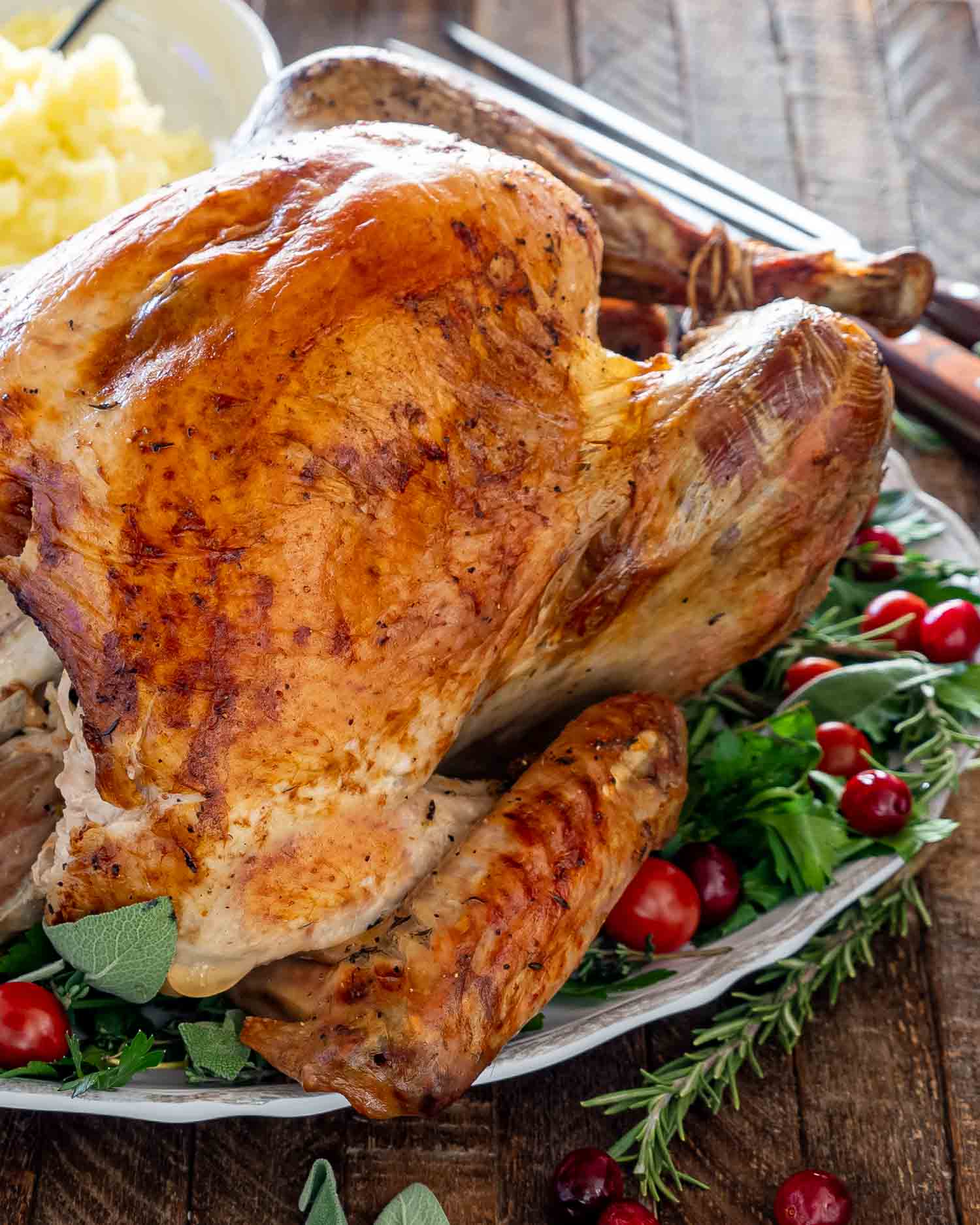 a roast turkey on a turkey platter garnished with herbs and cranberries.