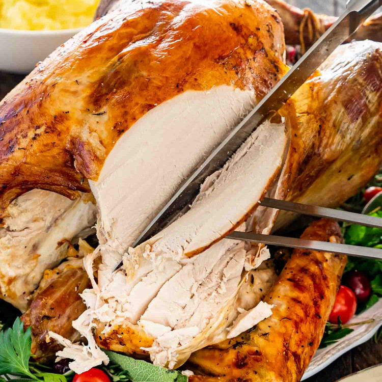 a hand carving turkey breast from a roast turkey.