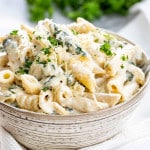 a serving of spinach artichoke pasta in a bowl garnished with parmesan cheese.