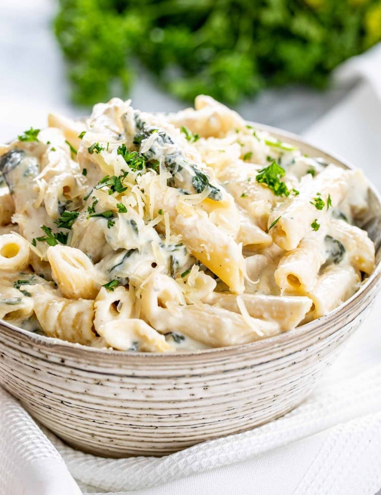 a serving of spinach artichoke pasta in a bowl garnished with parmesan cheese.