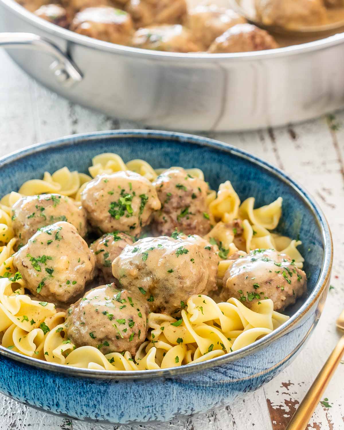 swedish meatballs with gravy over noodles in a blue bowl.